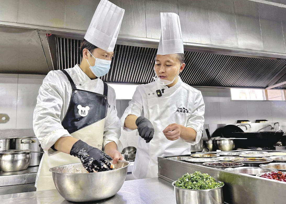 王友（右）給徒弟做菜品指導。魏慧敏、劉娟娟攝
